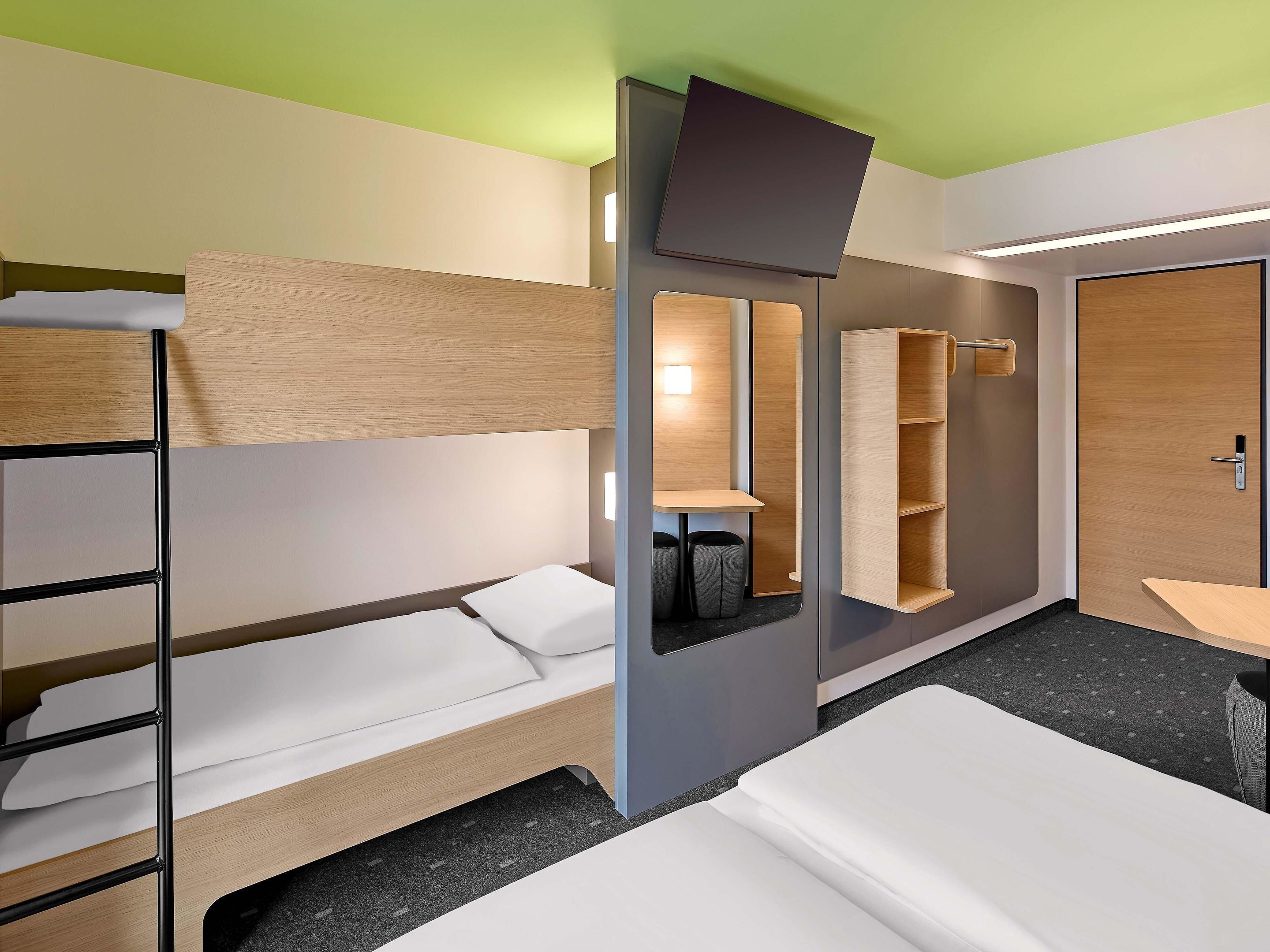 Een hotelkamer met stapelbedden, een bureau, een stoel, een spiegel en een kledingkast.