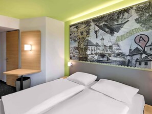 A hotel room with a bed, a nightstand, a wall-mounted lamp, and a large mural depicting a town scene. - B&B HOTEL Arnsberg (Arnsberg)