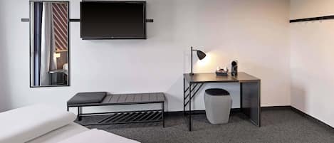 A modern hotel room with a bed, a desk, a chair, a TV, and a lamp.