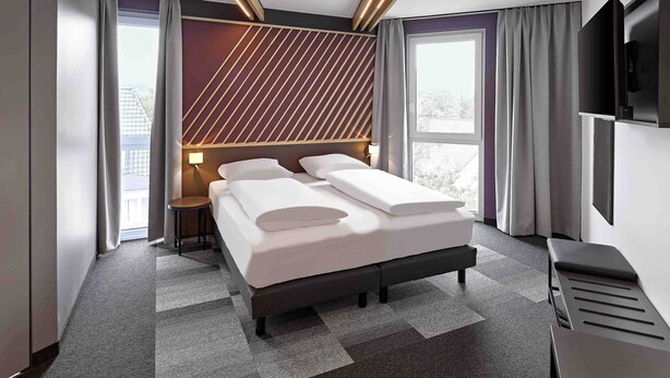 A modern hotel room with a large bed, a TV, and a view of the outside. - B&B HOTEL Arnsberg (Arnsberg)