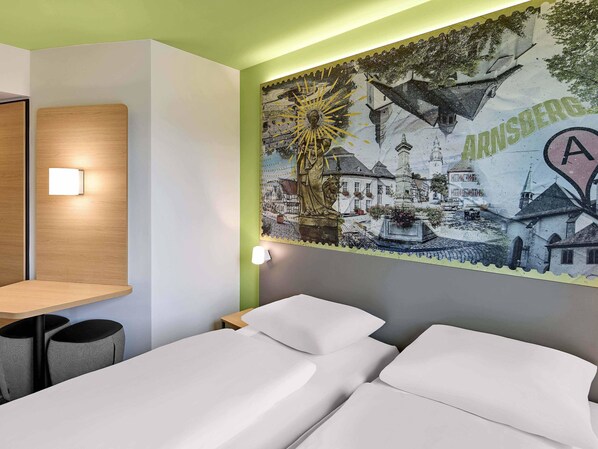 A hotel room with a bed, bedside tables, and a mural depicting a town scene.