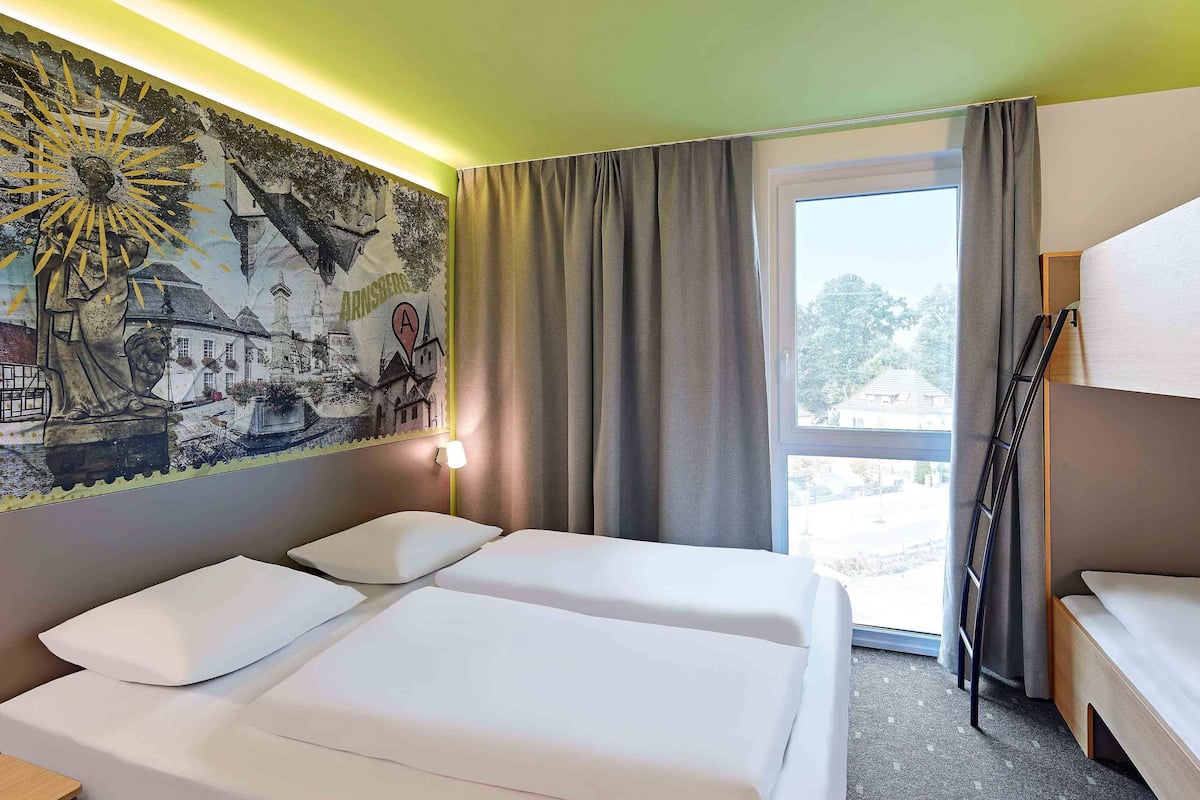 Ein Hotelzimmer mit zwei Betten, einem Wandgemälde, einem Fenster mit Vorhängen und Blick nach außen.