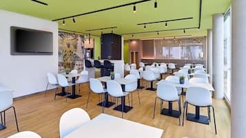 Uma sala de conferências moderna com mesas e cadeiras brancas, uma televisão de tela plana grande e um mural na parede.
