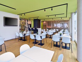 Una sala de conferencias moderna con mesas y sillas blancas, un televisor de pantalla plana grande y un mural en la pared.