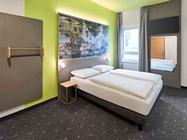 Habitación de hotel con cama, una mesita, un cuadro en la pared y una ventana con cortinas.