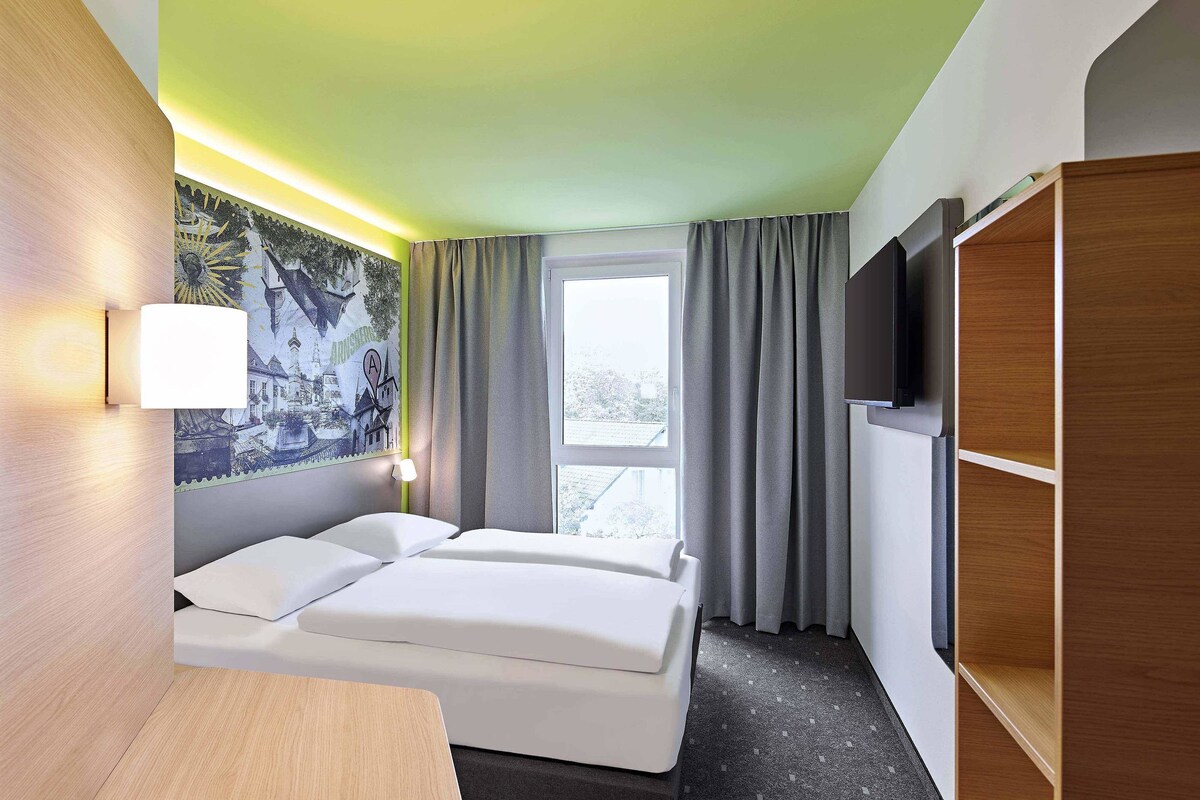 A hotel room with a bed, a desk, a TV, and a window with curtains.