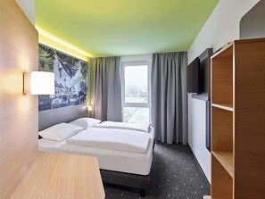 A hotel room with a bed, a desk, a TV, and a window with curtains. - B&B HOTEL Arnsberg (Arnsberg)