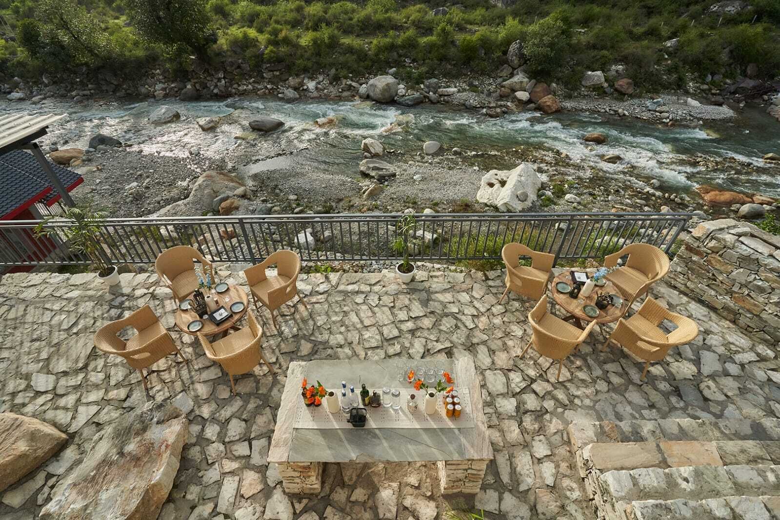 An outdoor seating area with stone flooring and wicker furniture overlooking a river.