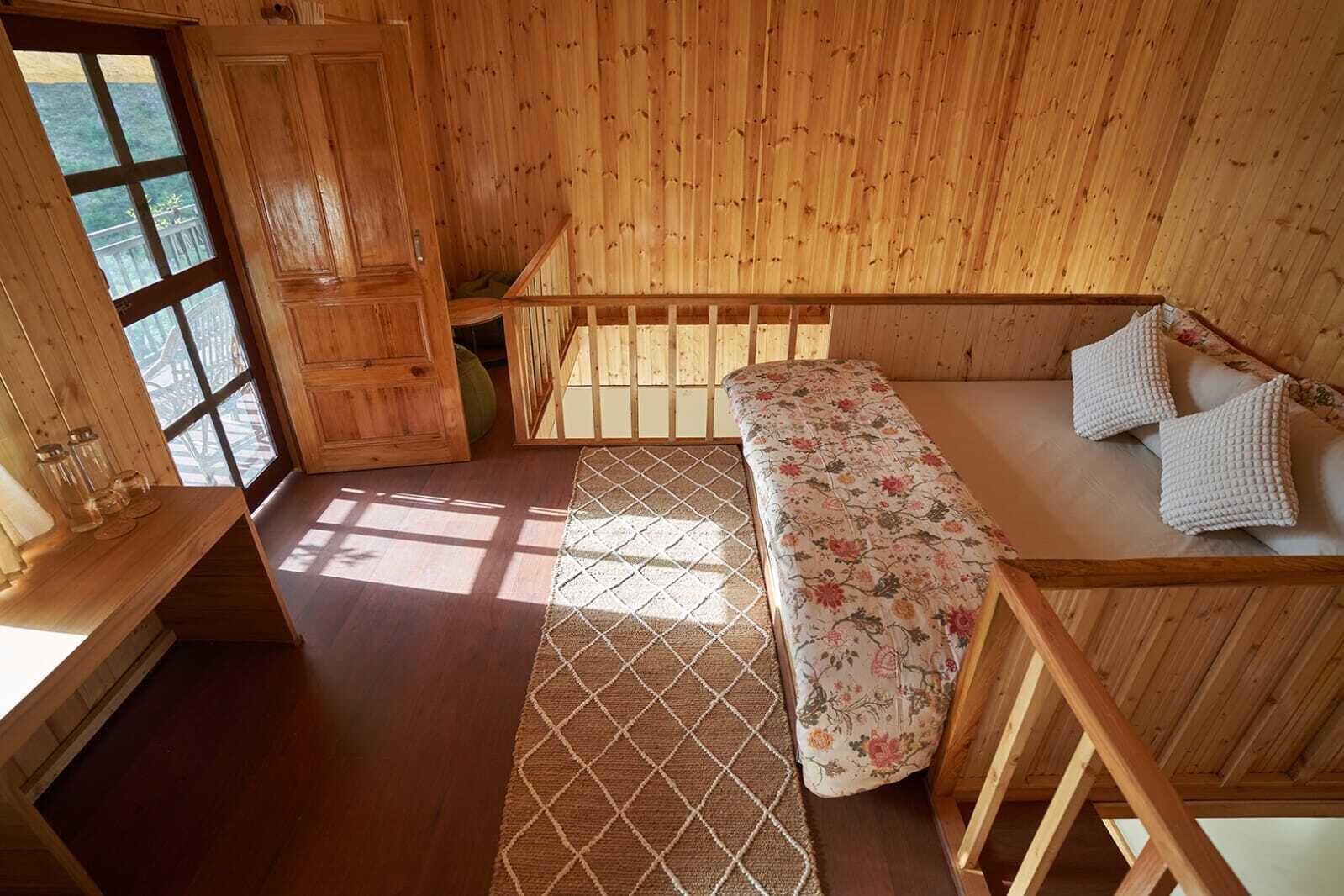 A wooden cabin interior with a bed, a window, and a wooden door.