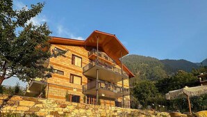 Un edificio de varios pisos con fachada de piedra, un balcón y un pequeño estanque con rocas y helechos en primer plano.