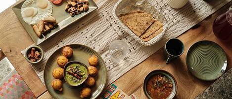 A breakfast table with eggs, tomatoes, mushrooms, chapatis, and a bowl of green chutney.