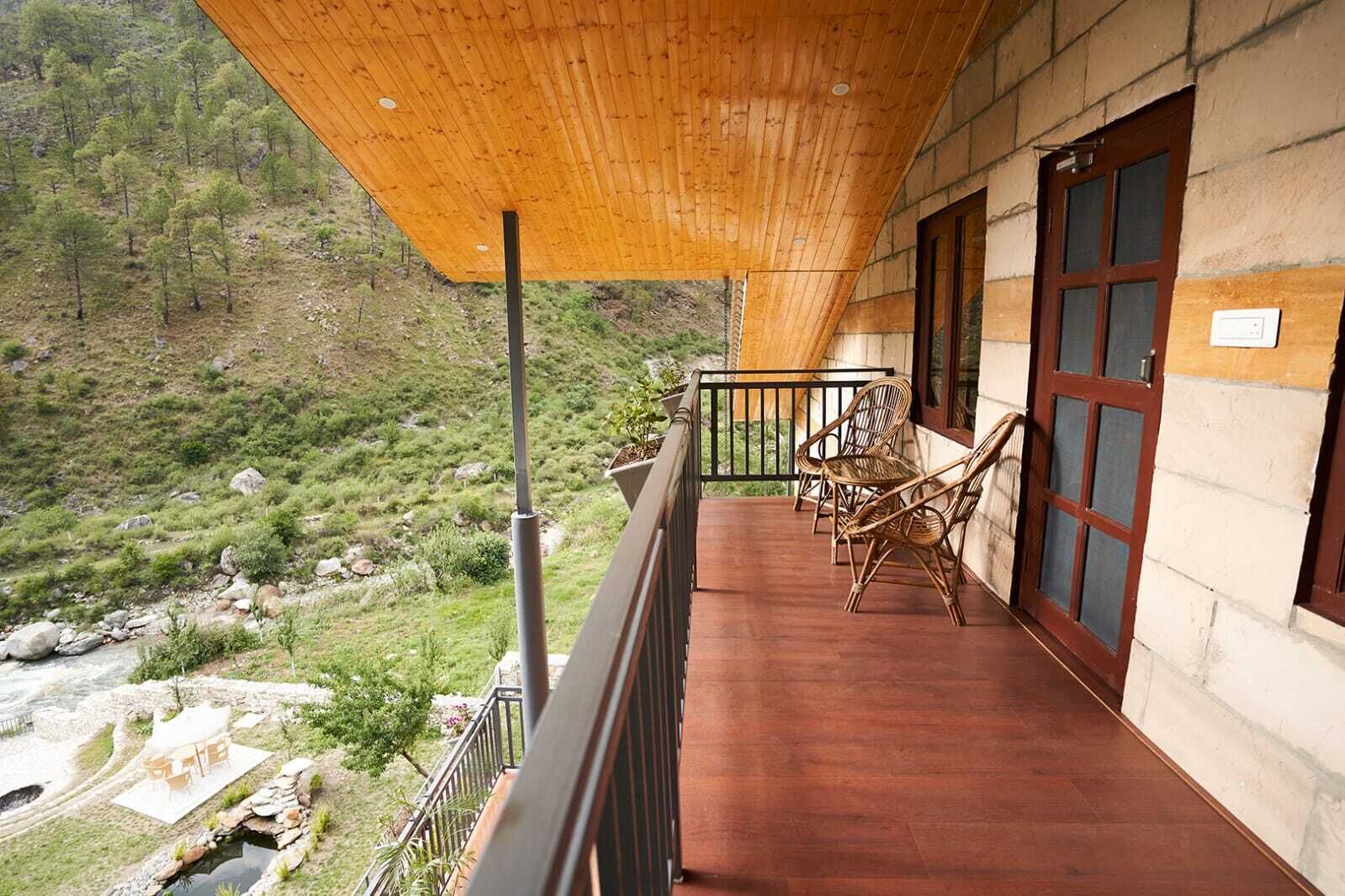 A wooden balcony with wicker chairs, overlooking a mountainous landscape.