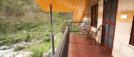 A wooden balcony with wicker chairs, overlooking a mountainous landscape.