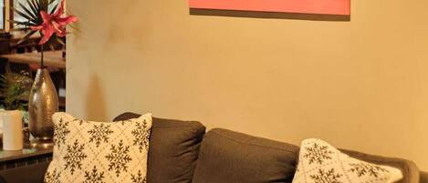 A living room with a brown sofa, two patterned pillows, and a wall-mounted painting of a fruit.