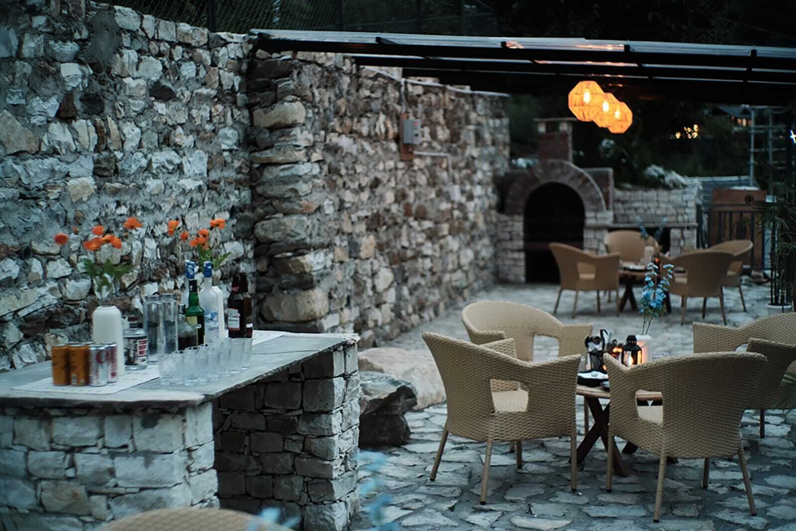 Un patio al aire libre con paredes de piedra, muebles de mimbre y un horno de piedra.