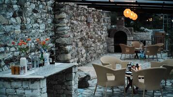 Un patio al aire libre con paredes de piedra, muebles de mimbre y un horno de piedra.
