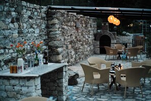 An outdoor patio with stone walls, wicker furniture, and a stone oven. - Mashru Riverside Estate (Banjar)