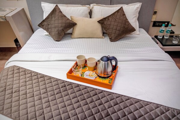 Una cama bien tendida con una colcha acolchada, dos almohadas y una mesita de noche con tazas, un hervidor y un vaso de agua.
