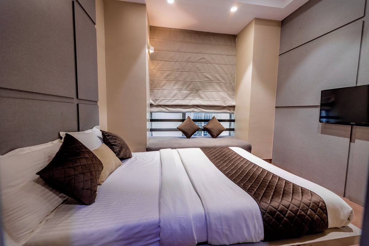 A modern hotel room with a large bed, a seating area with a view, and a flat-screen TV mounted on the wall.