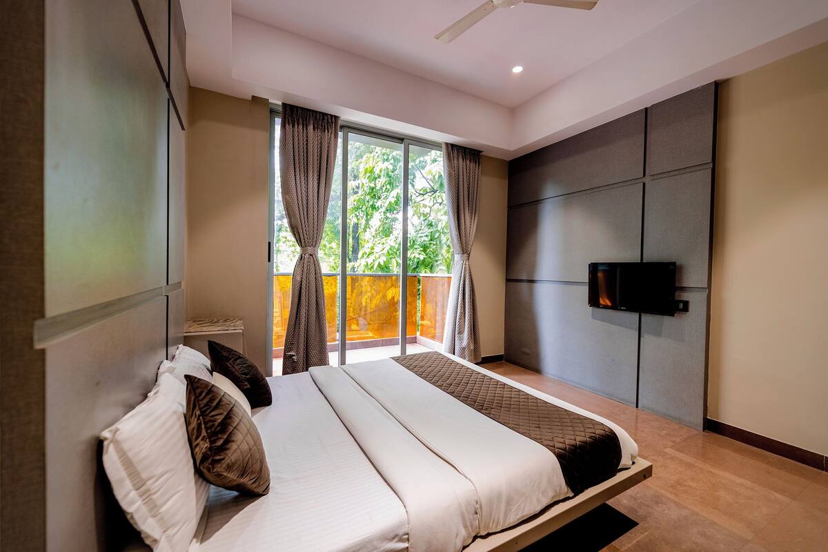 A modern bedroom with a large bed, a TV mounted on the wall, and a balcony with curtains.