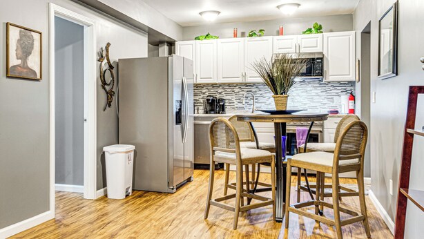 A modern kitchen with white cabinets, a stainless steel refrigerator, a wooden dining table with four chairs, and a potted plant on the counter. - 4 Mi to Dtwn Indianapolis: Quiet Apartment w/ Yard (Indianapolis)