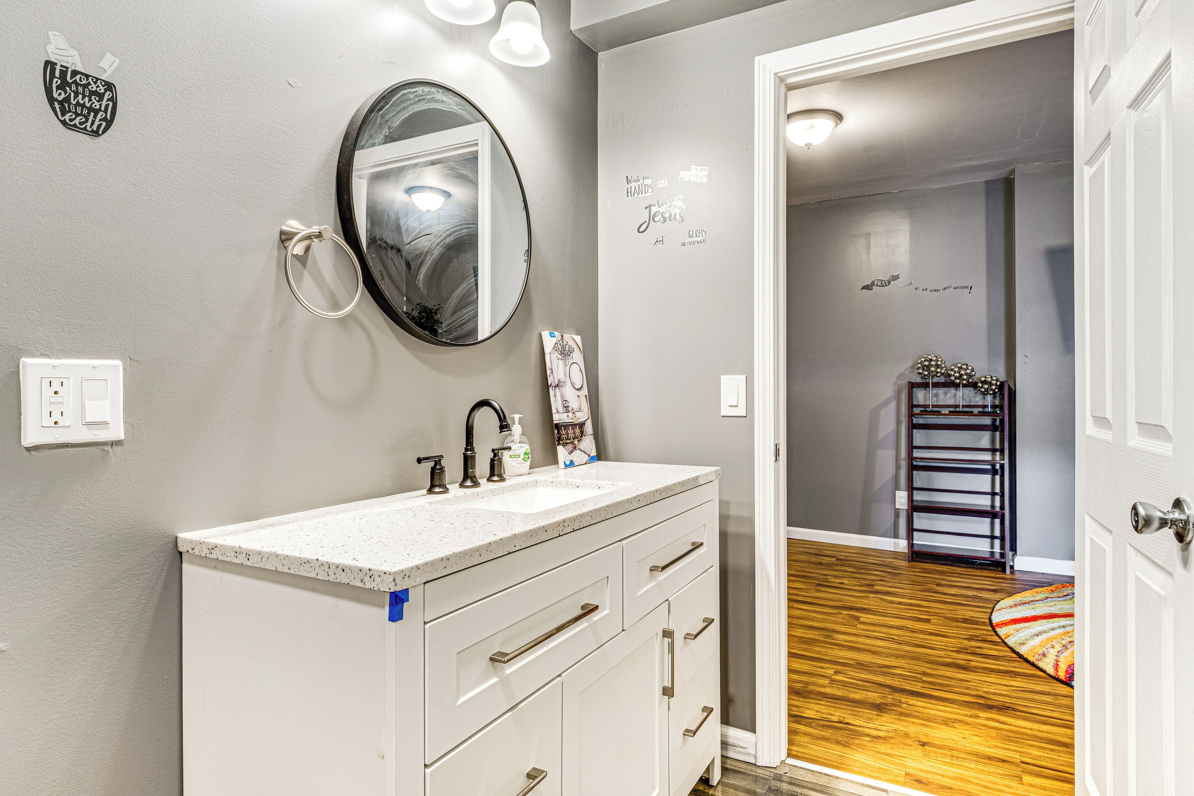 A bathroom with a white vanity, a round mirror, and a sink. There is a towel rack and a wall decal with text.
