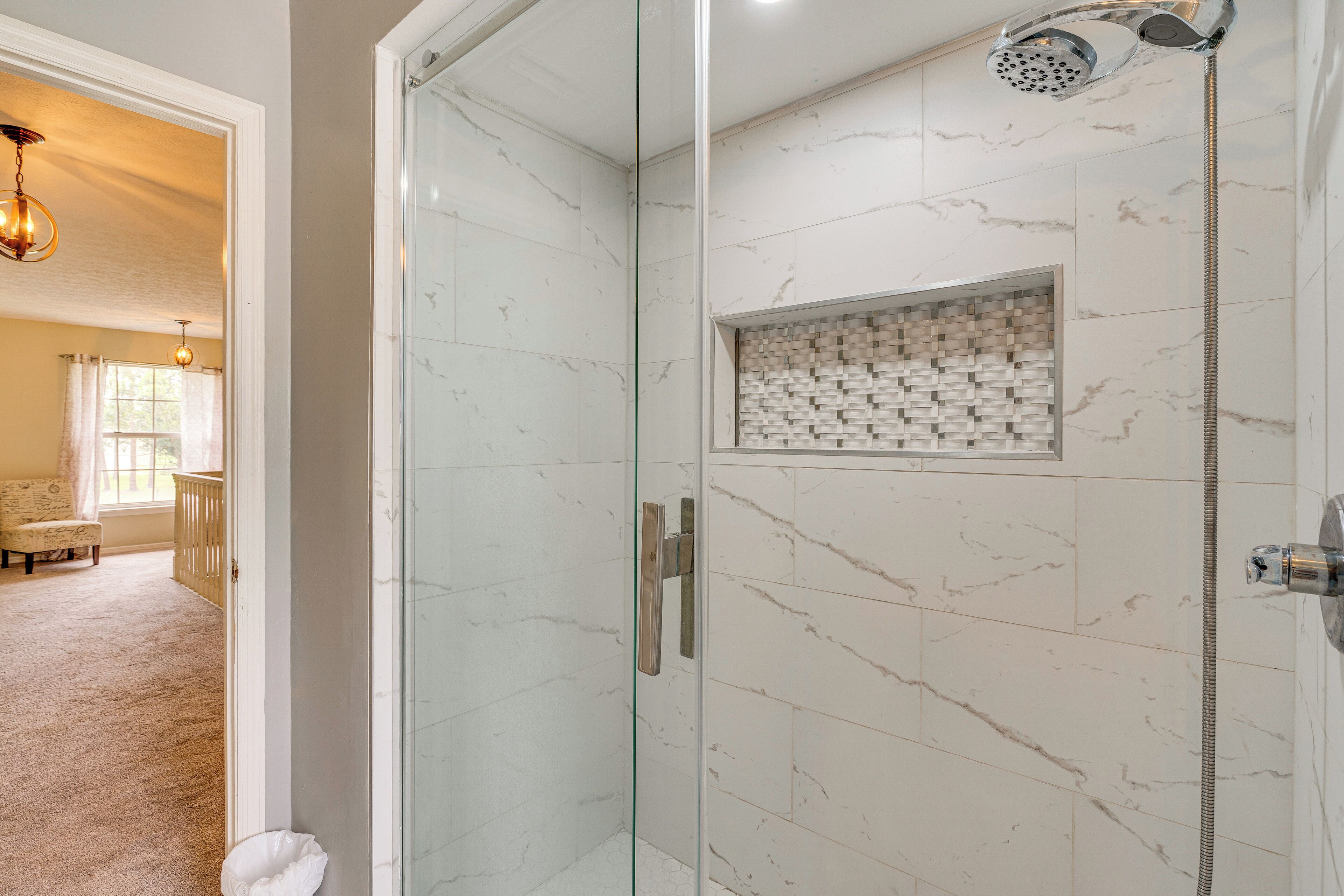 A bathroom with a glass-enclosed shower, marble tiles, and a small tiled accent wall.