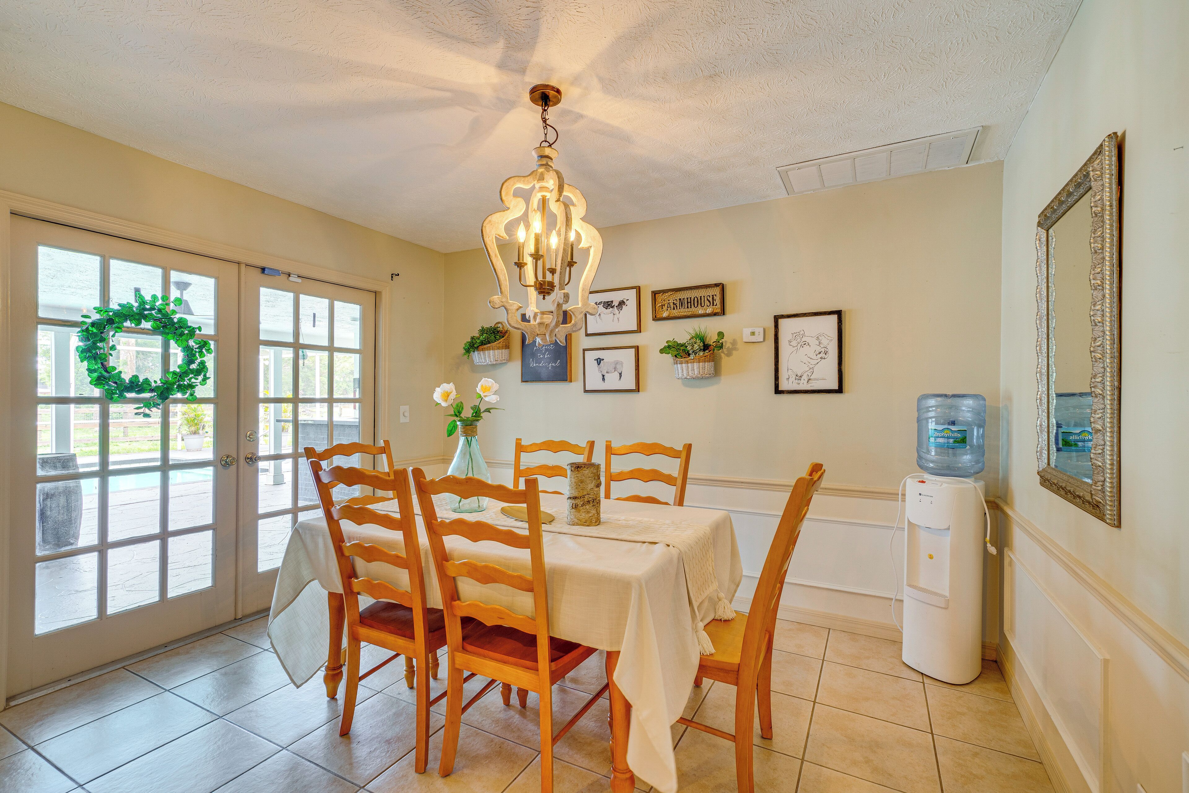 A dining area with a table set for four, wooden chairs, a chandelier, and a water dispenser.