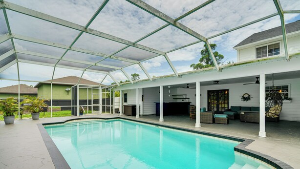 A covered swimming pool with a glass roof, surrounded by a patio area with seating and a view of a house in the background. - Private Pool & Yard: Family Retreat in Cape Coral (Cape Coral)