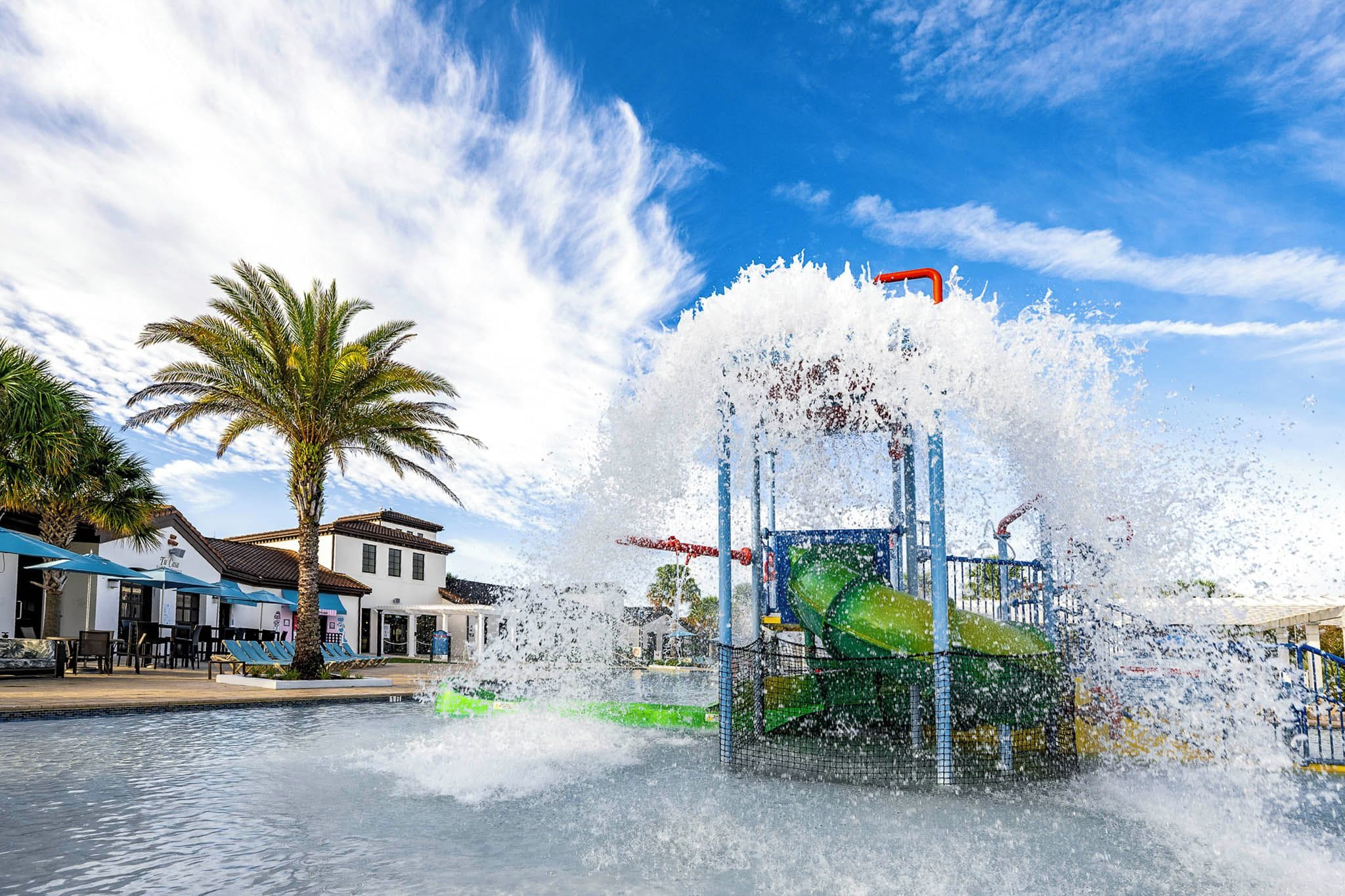 A water feature with a fountain and slides, surrounded by palm trees and a building with a sign that reads 'The Casa'.