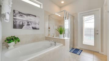 Une salle de bain moderne dotée d’une grande baignoire, d’une douche à parois de verre et d’une porte donnant sur un balcon.