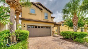 A two-story house with a garage, surrounded by lush greenery and palm trees. - Pool & Lazy River: Windsor House 9 Mi to Disney! (Kissimmee)