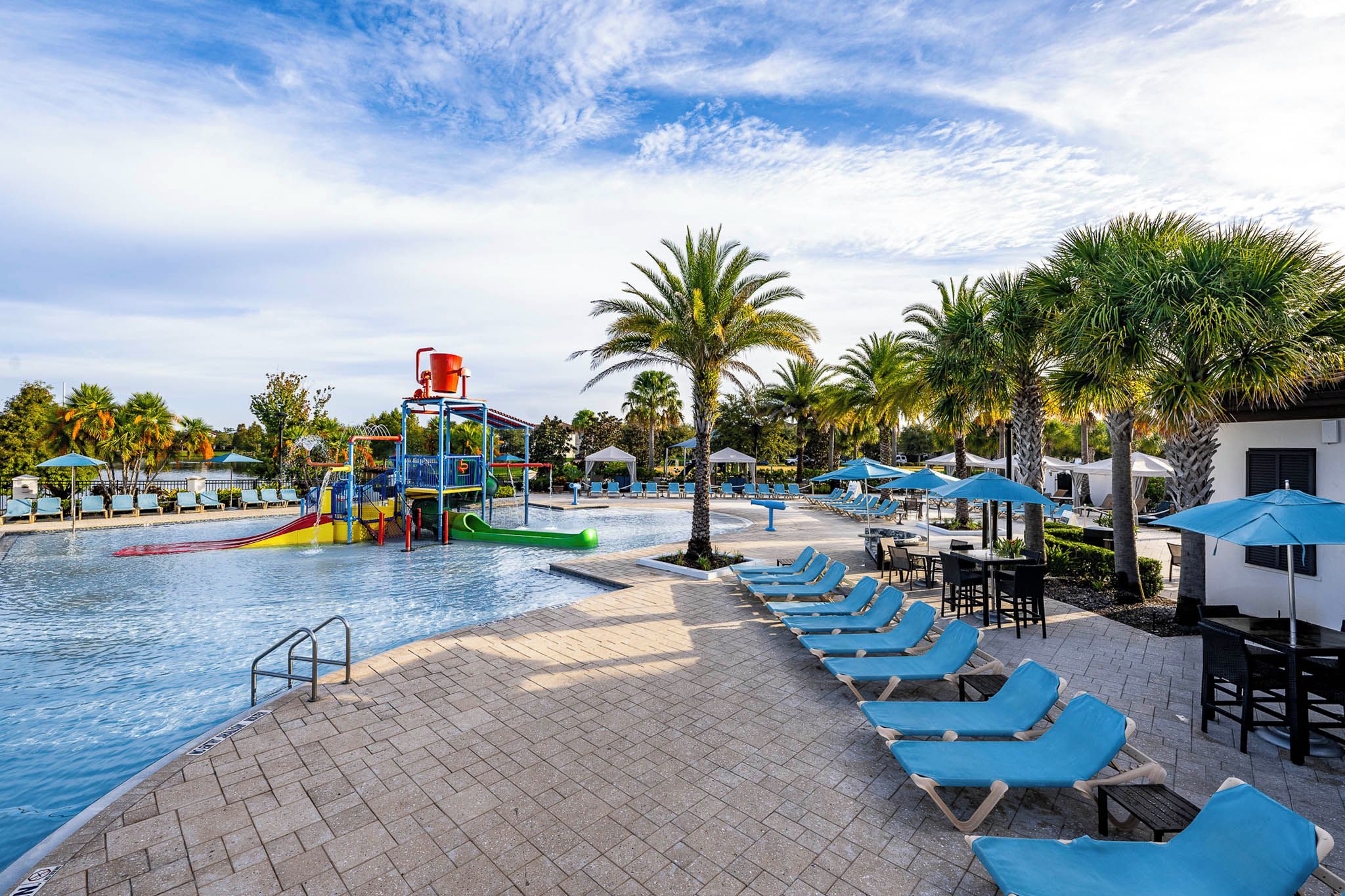A swimming pool area with a water slide, lounge chairs, and palm trees.
