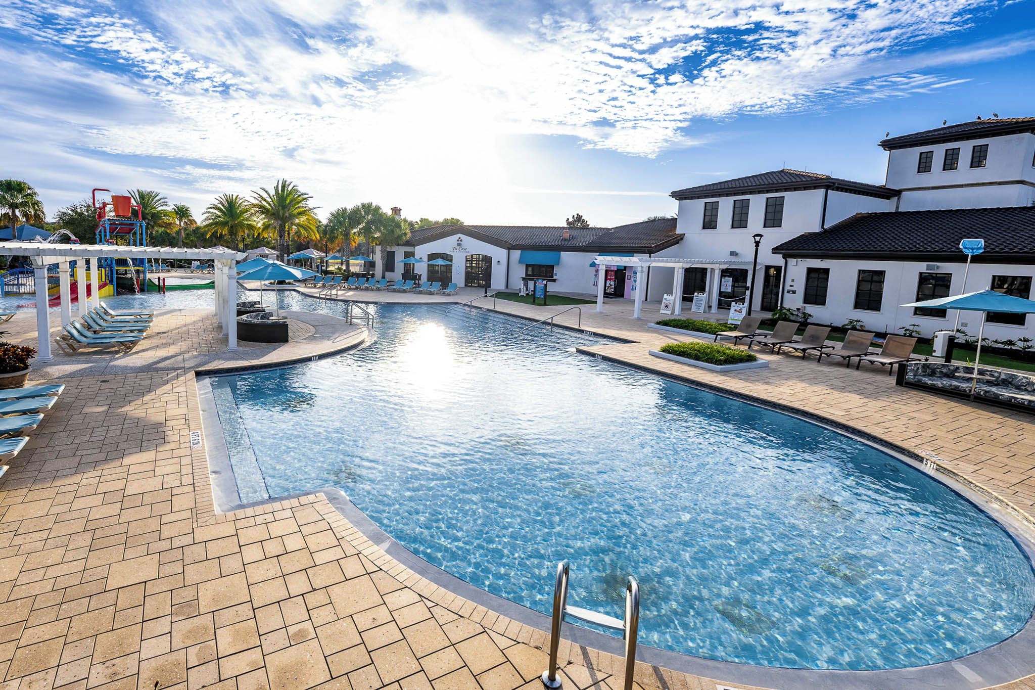 A swimming pool with a sunken center, surrounded by lounge chairs and umbrellas, with a building in the background.