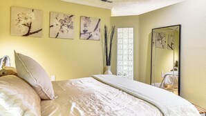 A neatly made bed with a white comforter and pillows, a vase with branches, and three floral wall art pieces. - Backs to Wetlands: Tranquil Beaverton Retreat! (Beaverton)