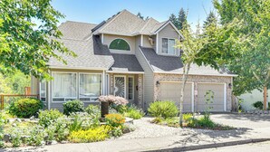 A two-story house with a garage, a front yard with various plants, and a clear blue sky. - Backs to Wetlands: Tranquil Beaverton Retreat! (Beaverton)