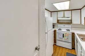 A compact kitchen with white cabinets, a refrigerator, an oven, and a sink.