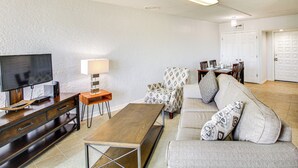Ein modernes Wohnzimmer mit Flachbildfernseher, Couchtisch aus Holz, gemustertem Sessel und einer Couch mit dekorativen Kissen.