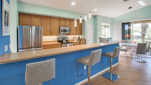 A modern kitchen with stainless steel appliances, a blue accent wall, and a bar area with bar stools. - 3 Mi to Dtwn Fort Myers: Condo w/ Pool & Hot Tub (North Fort Myers)
