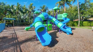 A playground with a blue and green slide structure, surrounded by palm trees and a clear sky. - 3 Mi to Dtwn Fort Myers: Condo w/ Pool & Hot Tub (North Fort Myers)