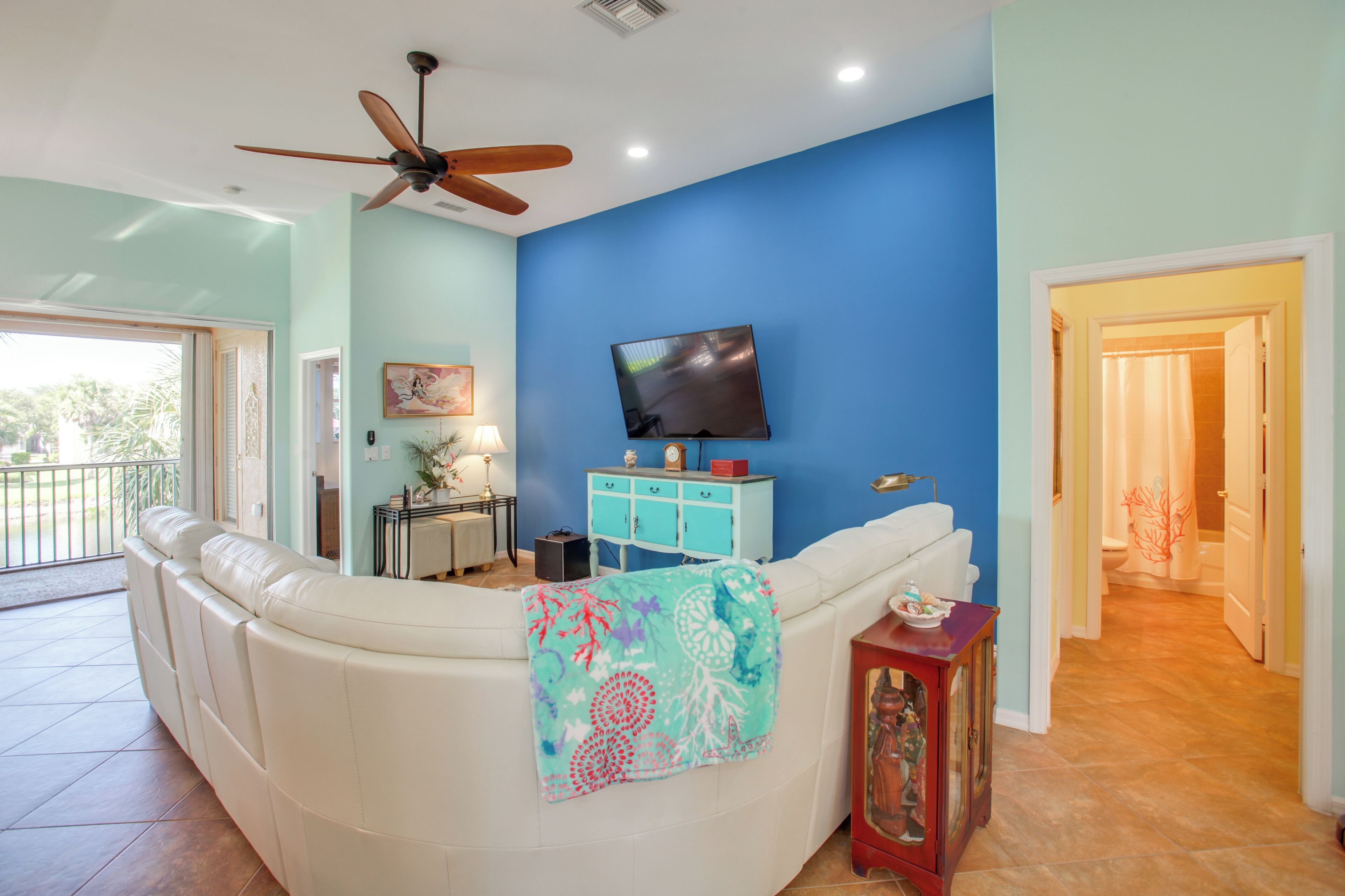 A living room with a white sofa, a ceiling fan, a TV, and a blue wall.