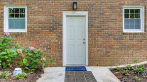 A brick building with a white door, two windows, and a blue mat at the entrance. - 5 Mi to Trilith Studios: Apt w/ Furnished Pergola (Fayetteville)