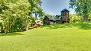 A large, two-story log cabin with a green roof, surrounded by lush greenery and trees. - White River Access & Views: Retreat w/ Shared Dock (Gassville)