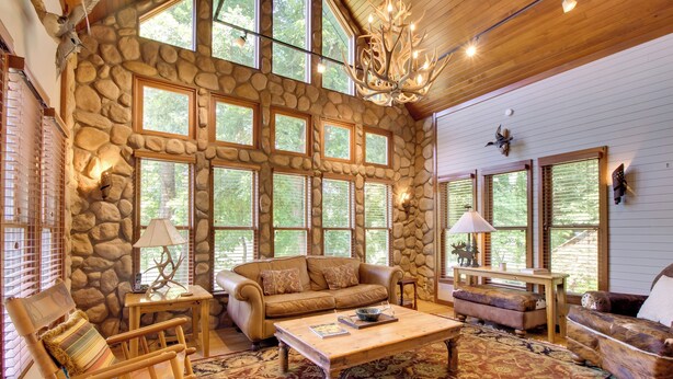 A spacious living room with a stone wall, large windows, and a chandelier. - White River Access & Views: Retreat w/ Shared Dock (Gassville)