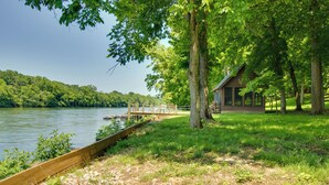A lakeside cabin with a dock extending into the water, surrounded by lush greenery and trees. - White River Access & Views: Retreat w/ Shared Dock (Gassville)