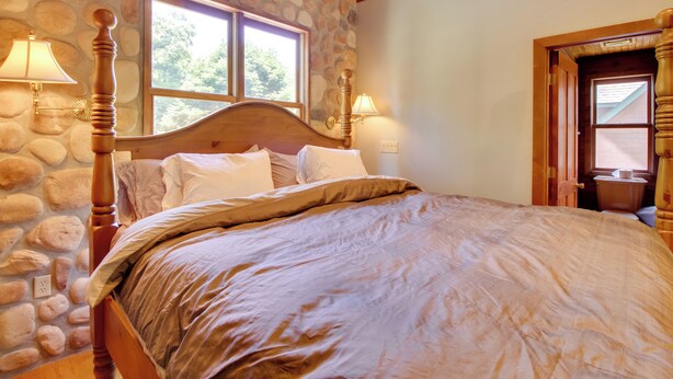 Un dormitorio con pared de piedra, estructura de cama de madera y dos lámparas de noche.