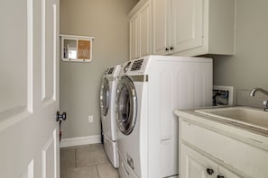 A laundry room with two front-loading washing machines, a small shelf with a mirror, and a sink with a faucet.