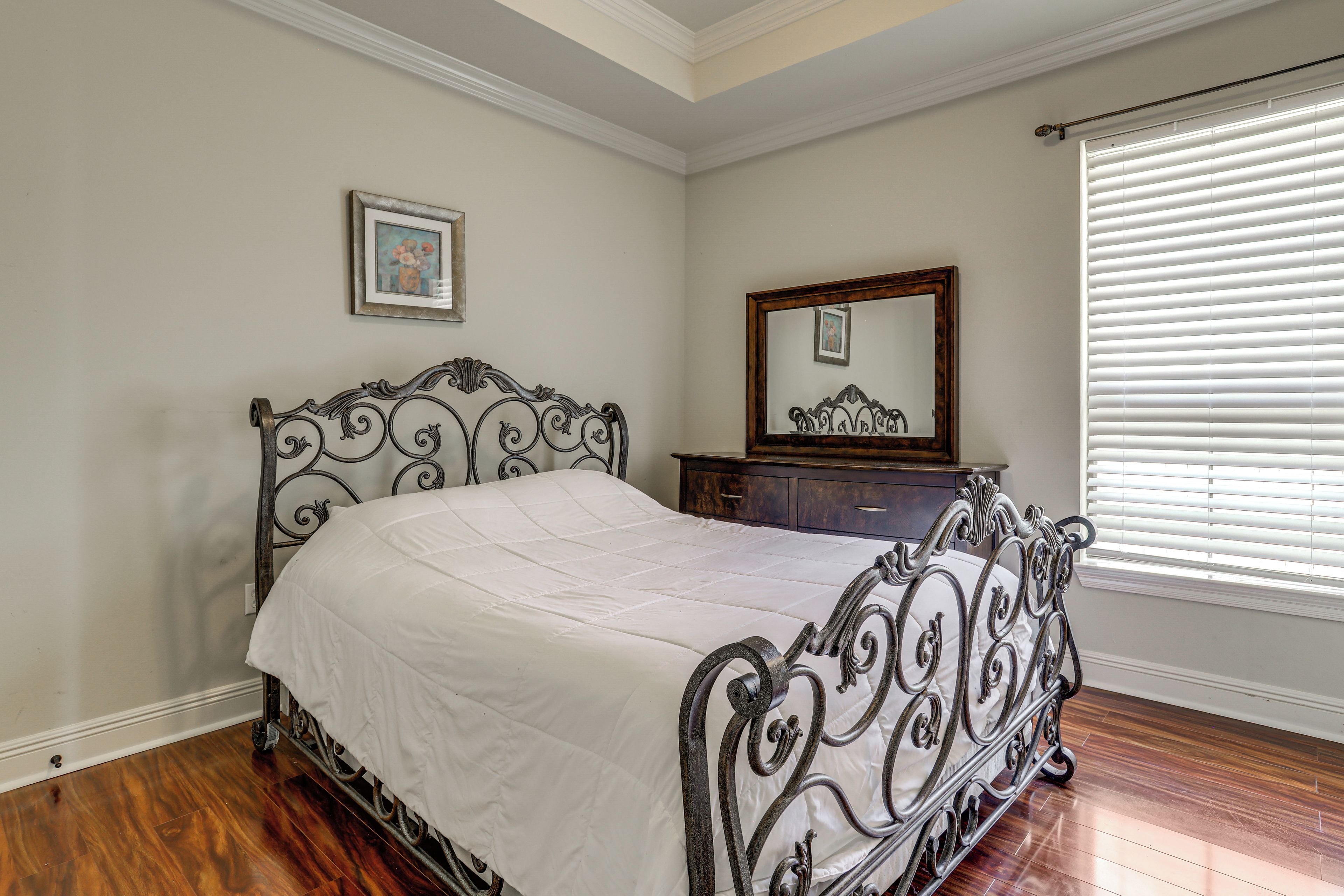 A bedroom with a bed, dresser, mirror, and a window with blinds.
