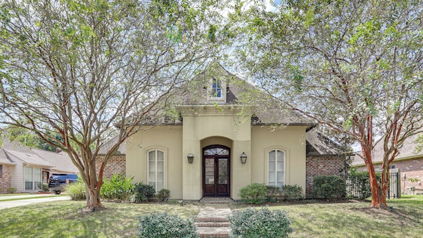 A two-story house with a brick facade, a dark brown front door, and a small porch with steps leading to it. - Easy Access to I-10: Prairieville Extended Stay (Prairieville)