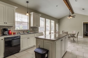 A kitchen with white cabinets, a dishwasher, a coffee maker, and a dining area with a table and chairs.